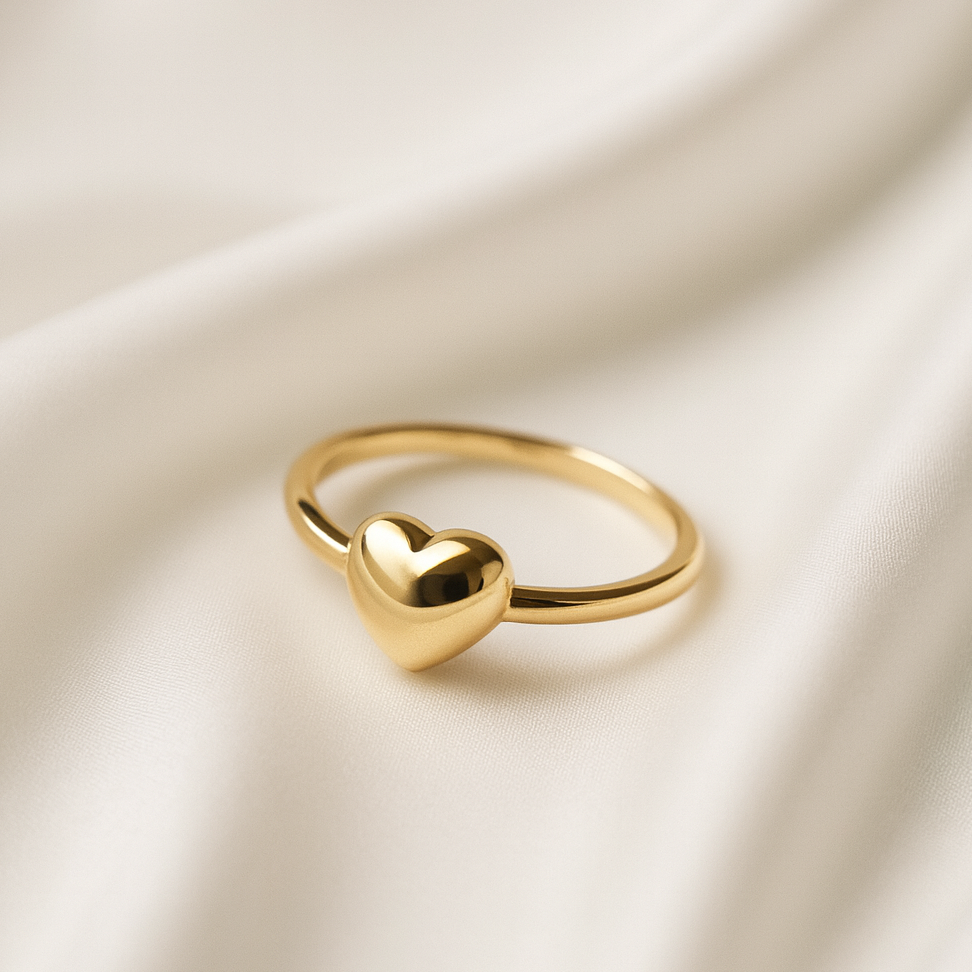 Pureheart 18 Carat Gold Sculpted Heart Ring – Masaira Gold band ring with a polished heart centerpiece placed on a textured ivory surface